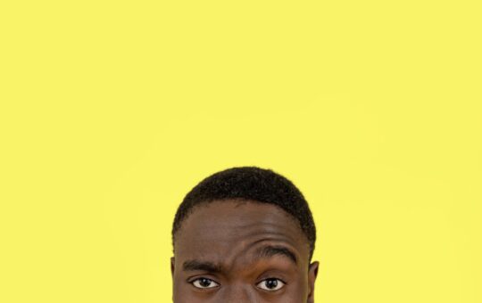 man raising eye on yellow studio background